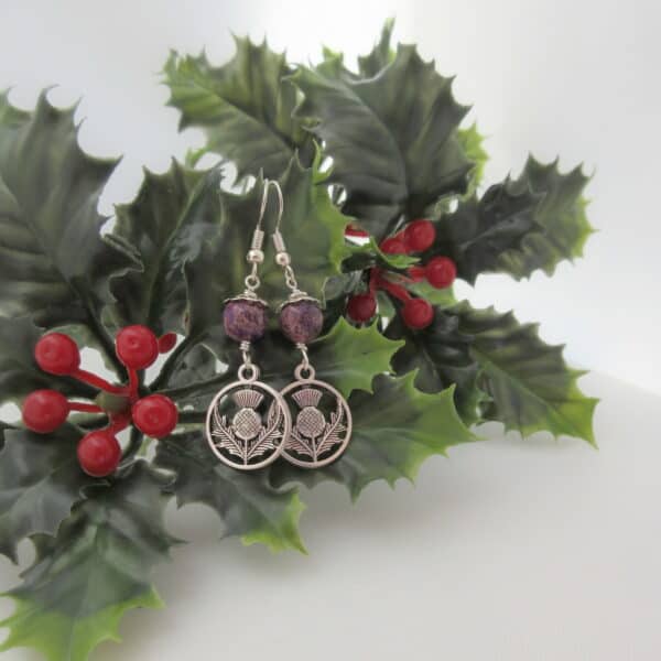 Drop earrings with silver coloured thistle charm and round purple jasper bead.